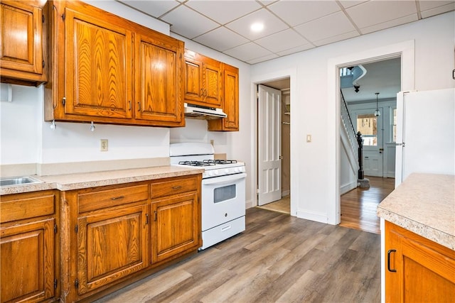 kitchen with brown cabinetry, light countertops, under cabinet range hood, and white appliances