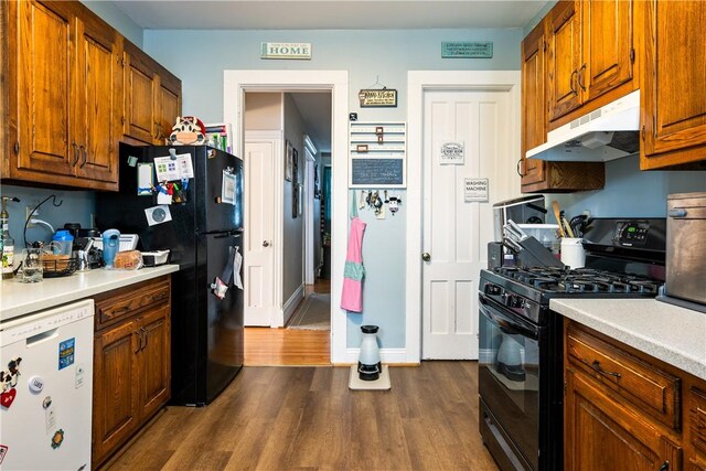 kitchen with light countertops, under cabinet range hood, black appliances, and dark wood-style floors