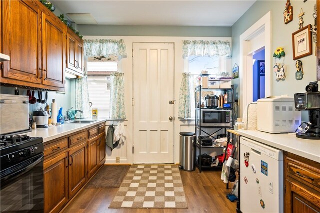 kitchen with light countertops, black gas range oven, a sink, and dark wood-type flooring