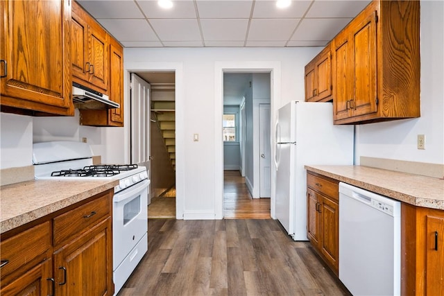 kitchen featuring white appliances, light countertops, under cabinet range hood, brown cabinets, and dark wood finished floors