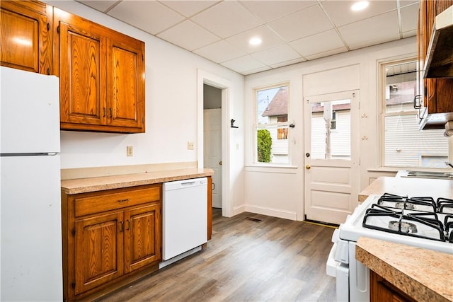 kitchen featuring dark wood-style flooring, white appliances, light countertops, brown cabinetry, and under cabinet range hood
