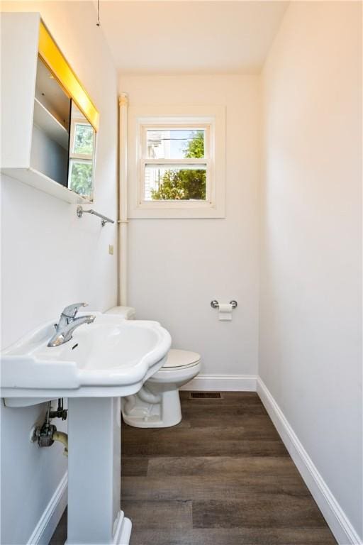 half bath featuring baseboards, toilet, wood finished floors, and visible vents