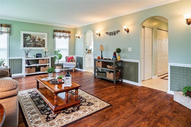 living area with arched walkways, baseboards, ornamental molding, and wood finished floors