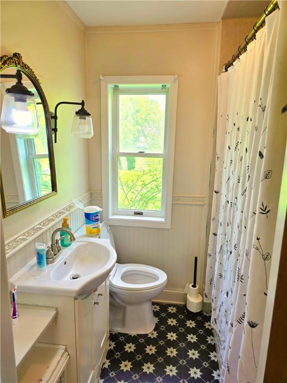 full bathroom with a wainscoted wall, plenty of natural light, toilet, and tile patterned floors
