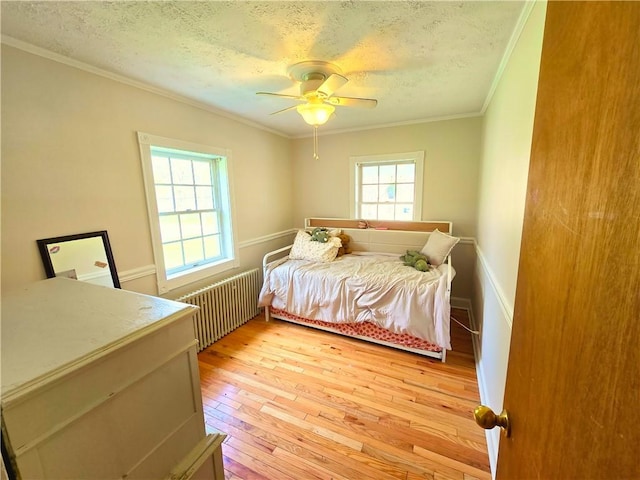 bedroom with crown molding, a textured ceiling, radiator heating unit, light wood-style flooring, and a ceiling fan