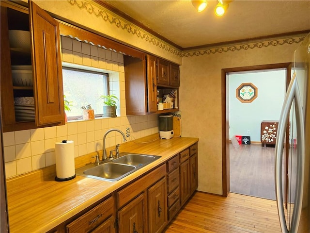 kitchen with brown cabinets, a sink, light wood-style floors, light countertops, and decorative backsplash
