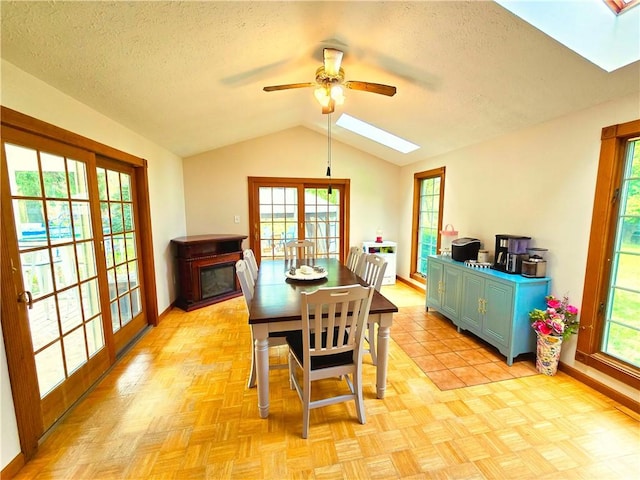 dining space featuring baseboards, lofted ceiling with skylight, a textured ceiling, and ceiling fan