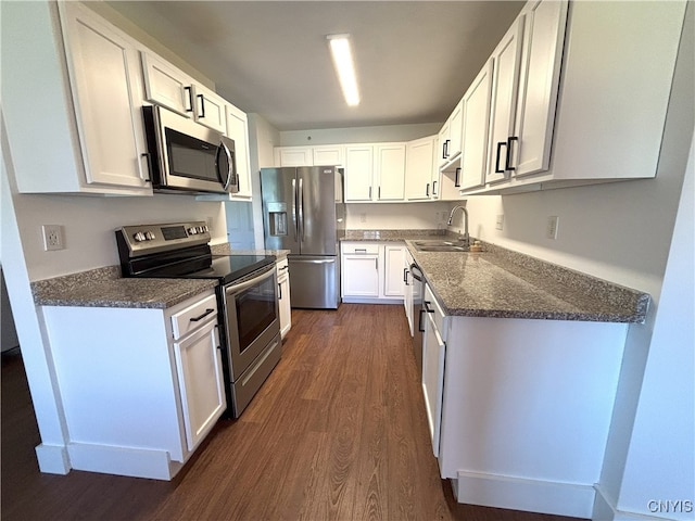 kitchen with dark wood-style flooring, a sink, dark stone counters, stainless steel appliances, and white cabinetry