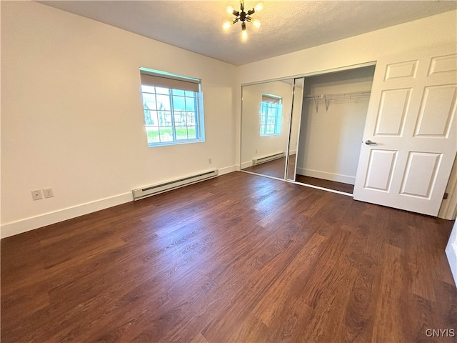 unfurnished bedroom featuring dark wood-type flooring, a baseboard heating unit, a chandelier, and a closet