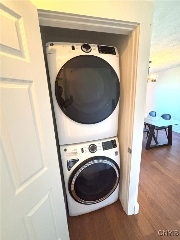 laundry area featuring a textured ceiling, laundry area, stacked washer and dryer, and wood finished floors