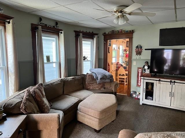 carpeted living area featuring ceiling fan and a drop ceiling