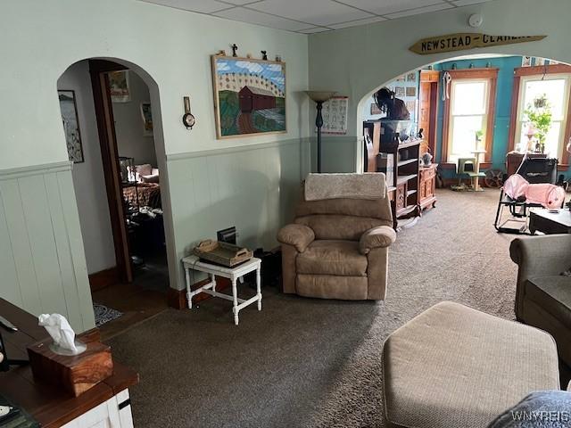 living room with carpet floors, arched walkways, and wainscoting
