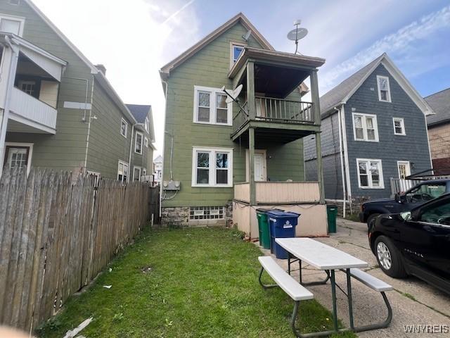 rear view of house with a yard, fence, and a balcony