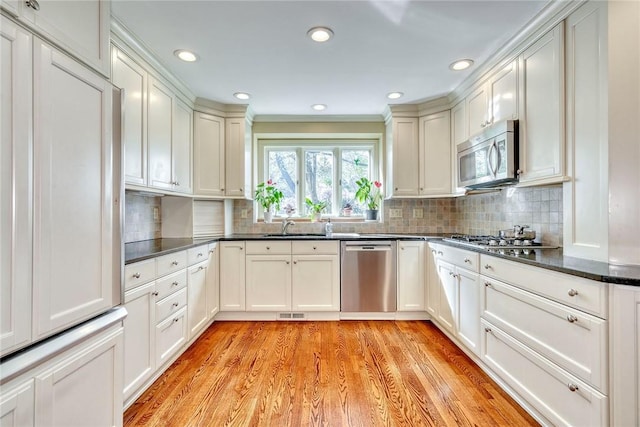 kitchen with light wood-type flooring, a sink, backsplash, and stainless steel appliances