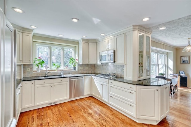 kitchen featuring a healthy amount of sunlight, appliances with stainless steel finishes, ornamental molding, and light wood-type flooring