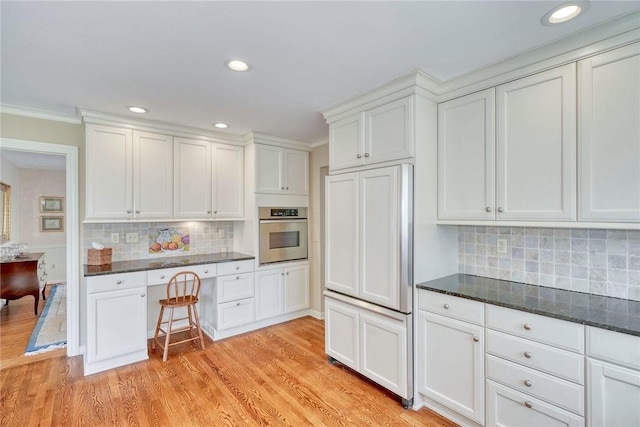 kitchen with oven, paneled built in fridge, light wood-style flooring, white cabinetry, and backsplash