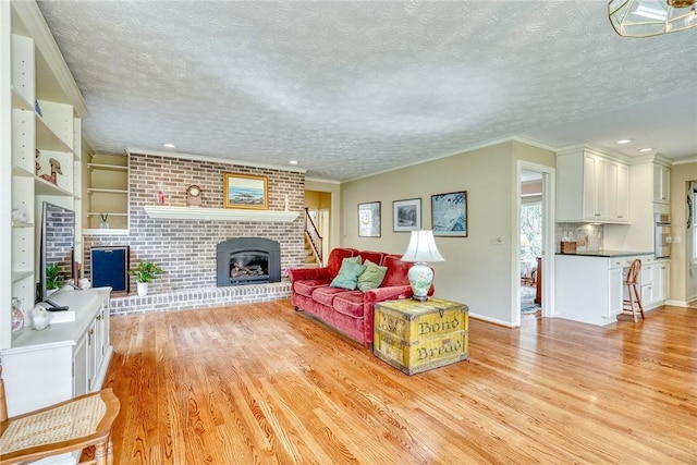 living area featuring a brick fireplace, a textured ceiling, ornamental molding, and light wood-style flooring