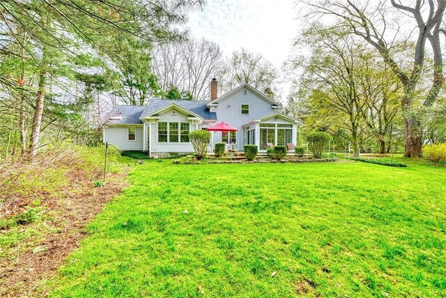 rear view of house featuring a lawn, a chimney, and a sunroom