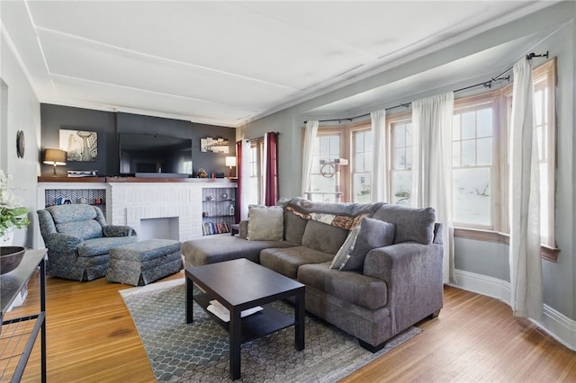 living area with a fireplace, baseboards, crown molding, and wood-type flooring