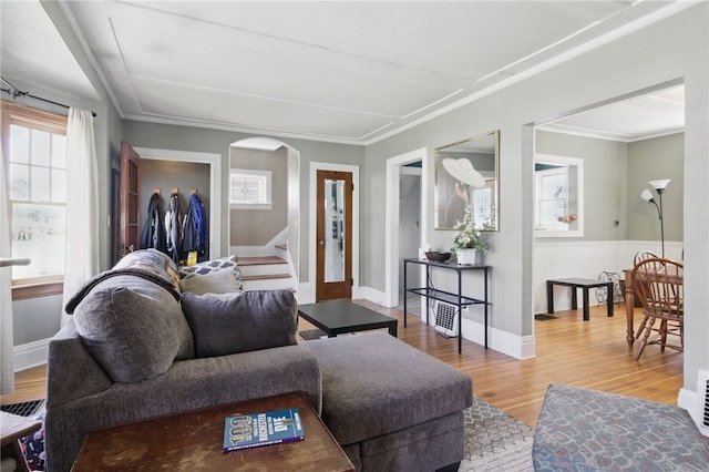 living room featuring crown molding, arched walkways, stairs, baseboards, and wood finished floors