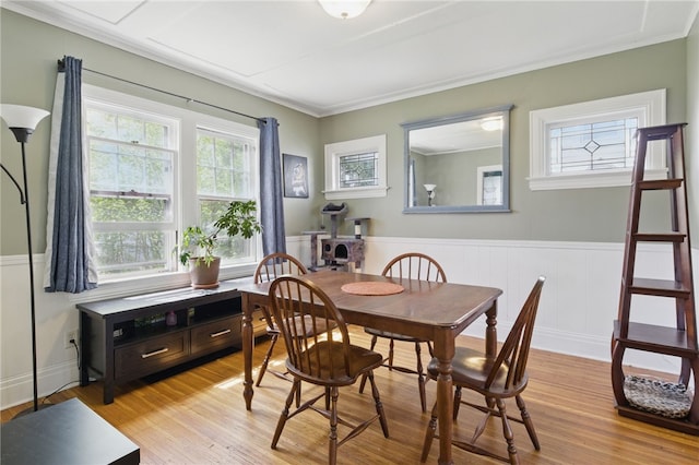 dining space featuring crown molding, a decorative wall, wainscoting, and light wood-style floors