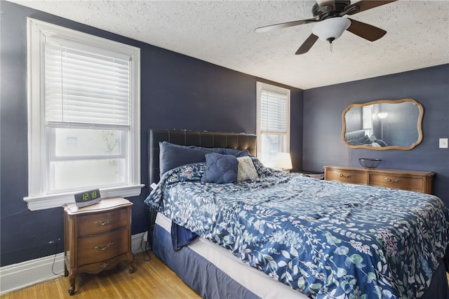 bedroom featuring baseboards, multiple windows, a textured ceiling, and wood finished floors