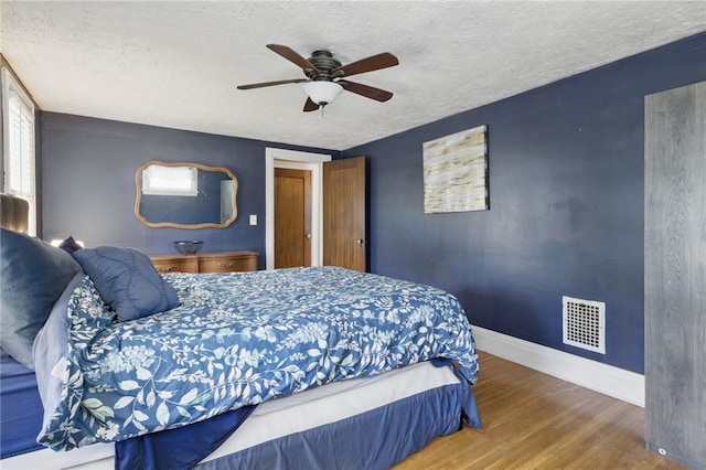 bedroom with a textured ceiling, a ceiling fan, baseboards, wood finished floors, and visible vents