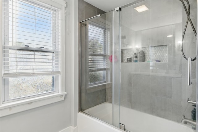 bathroom featuring shower / bath combination with glass door, baseboards, and plenty of natural light