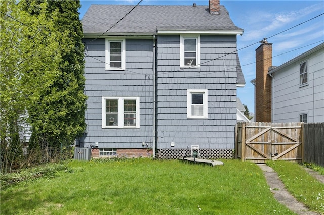 back of house featuring fence, a chimney, a yard, and roof with shingles