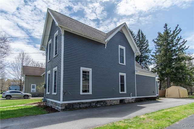 view of home's exterior with a storage unit, aphalt driveway, and an outbuilding