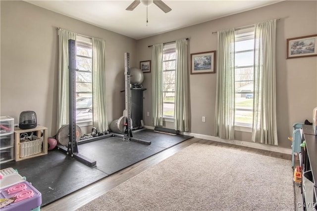 workout area featuring baseboards, ceiling fan, a healthy amount of sunlight, and wood finished floors