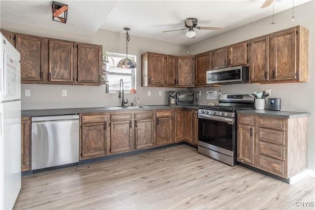 kitchen featuring ceiling fan, appliances with stainless steel finishes, dark countertops, a sink, and light wood finished floors