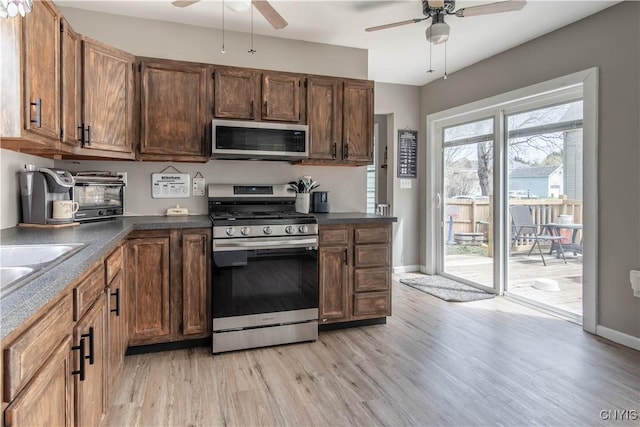 kitchen with stainless steel appliances, a ceiling fan, dark countertops, and light wood-style flooring