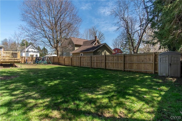 view of yard with a deck, an outdoor structure, a fenced backyard, a playground, and a storage unit