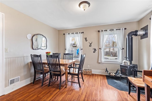 dining space featuring baseboards, a wood stove, wood finished floors, and visible vents