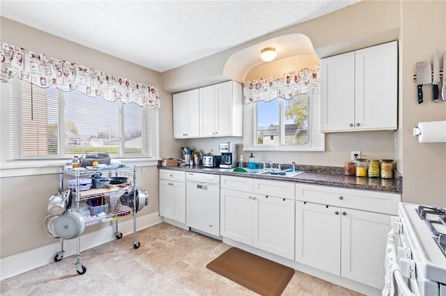 kitchen featuring a sink, dark countertops, white appliances, and white cabinetry
