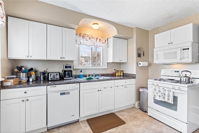 kitchen with white appliances, white cabinetry, a sink, and dark stone countertops