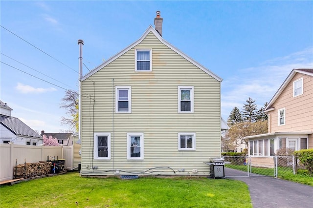 back of house with a lawn, fence, and a chimney