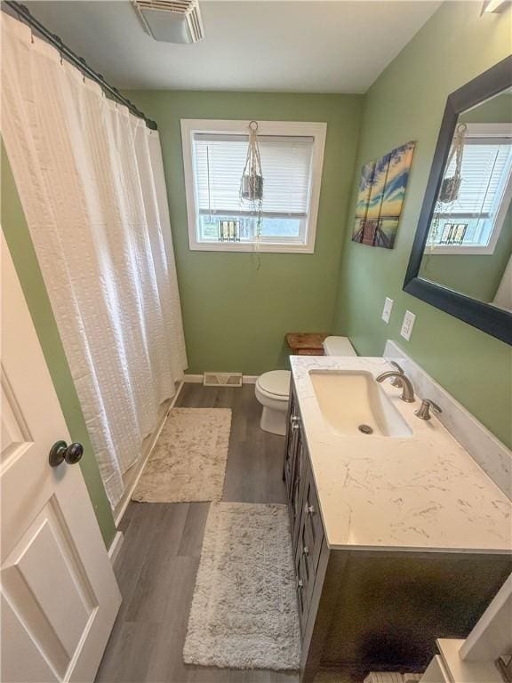 bathroom with visible vents, vanity, wood finished floors, toilet, and baseboards