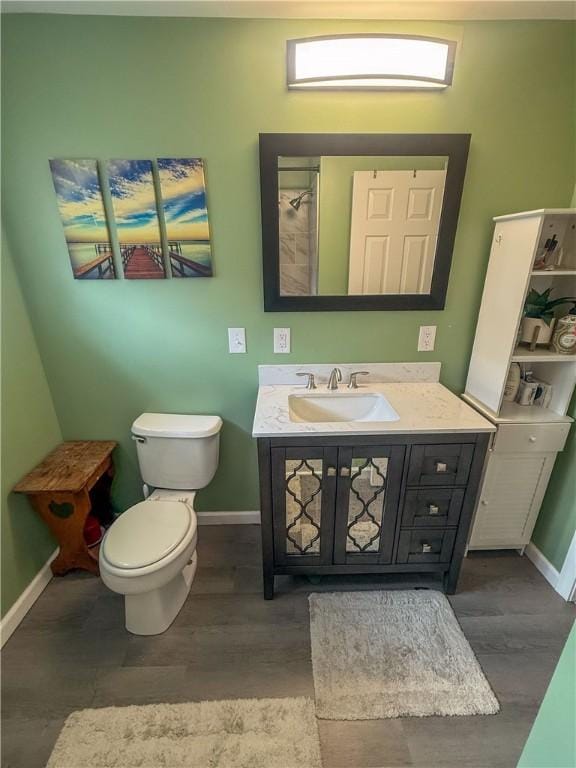 bathroom featuring a shower, wood finished floors, baseboards, vanity, and toilet