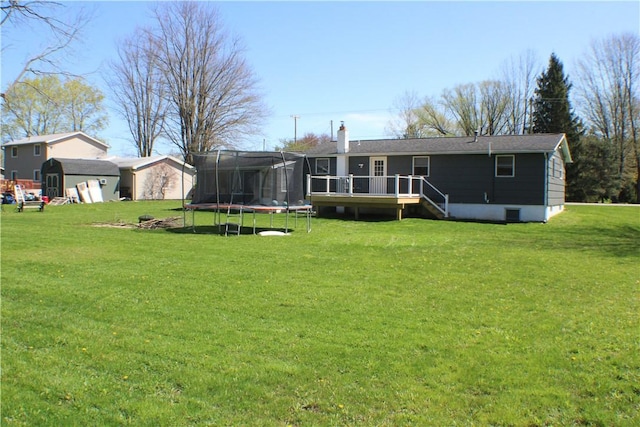 rear view of house featuring a lawn, a deck, a chimney, and a trampoline