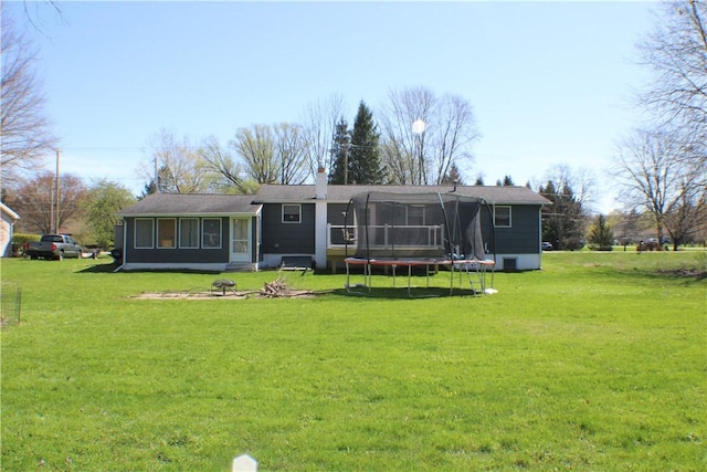 rear view of house featuring a sunroom, a trampoline, and a lawn