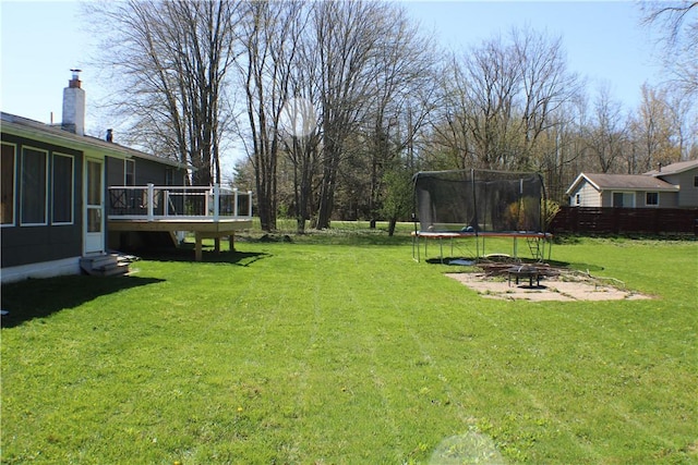 view of yard featuring fence, a wooden deck, and a trampoline