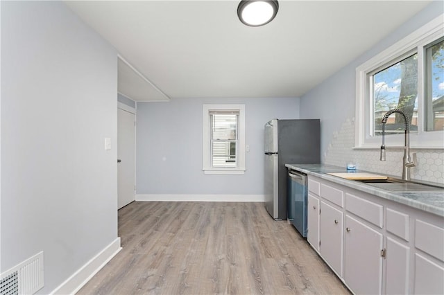 kitchen with a sink, light wood-style floors, backsplash, stainless steel dishwasher, and visible vents