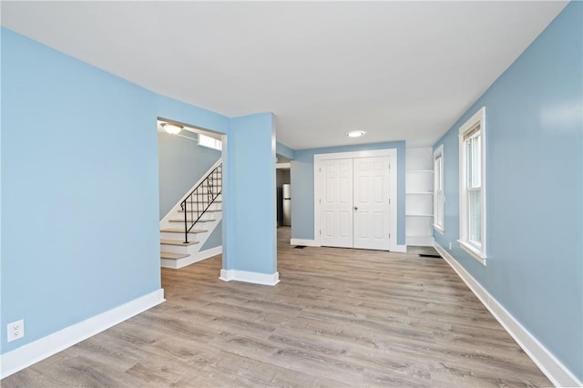 unfurnished living room featuring baseboards, stairs, and wood finished floors