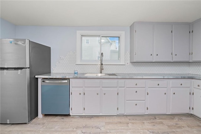 kitchen with a sink, light countertops, freestanding refrigerator, and dishwasher