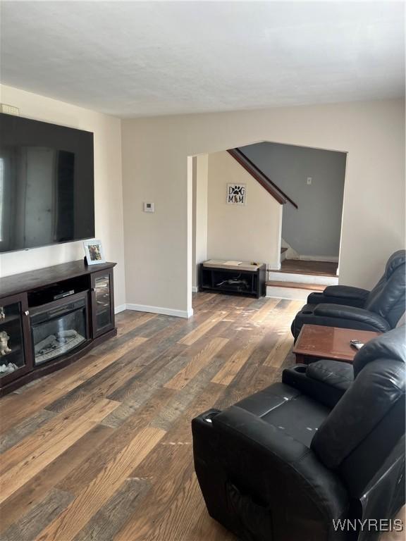 living room with stairs, dark wood-style flooring, and baseboards