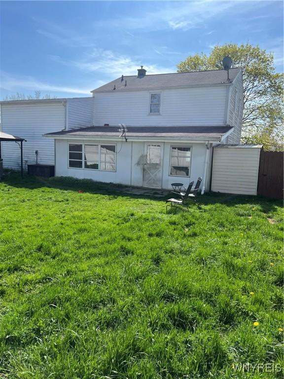 rear view of property featuring a lawn and fence