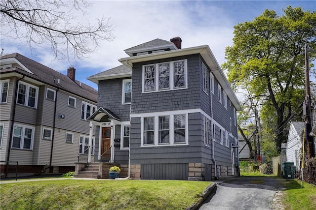 view of front facade featuring entry steps, a chimney, and a front yard