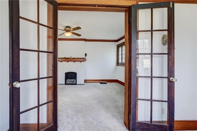 interior space with ceiling fan, a brick fireplace, baseboards, ornamental molding, and carpet